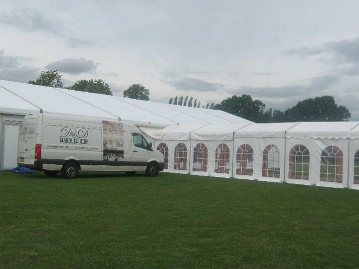 White van parked near a large white tent on a grassy field under a cloudy sky.