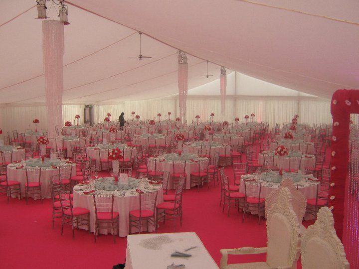 Pink-carpeted wedding reception tent, round tables with floral centerpieces, pink chairs, and white tablecloths.