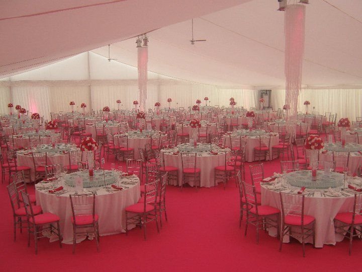 Large tent interior set for event, pink carpet, tables, chairs, and centerpieces.