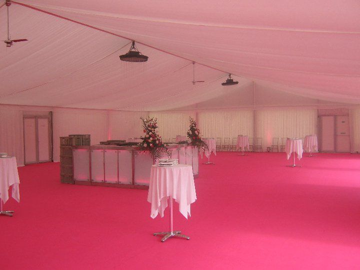 Inside event tent with pink carpet, white walls and ceiling, tables with white tablecloths, and a bar.