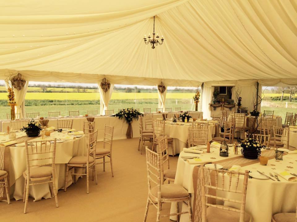 Wedding reception tent, ivory interior, round tables set, chairs, overlooking field of yellow.