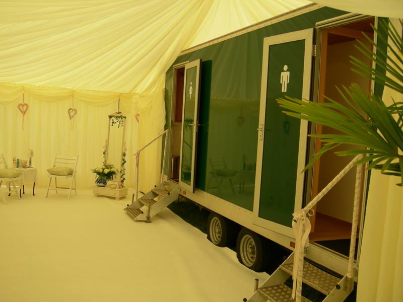 Green mobile restroom trailer with steps inside a white tent.