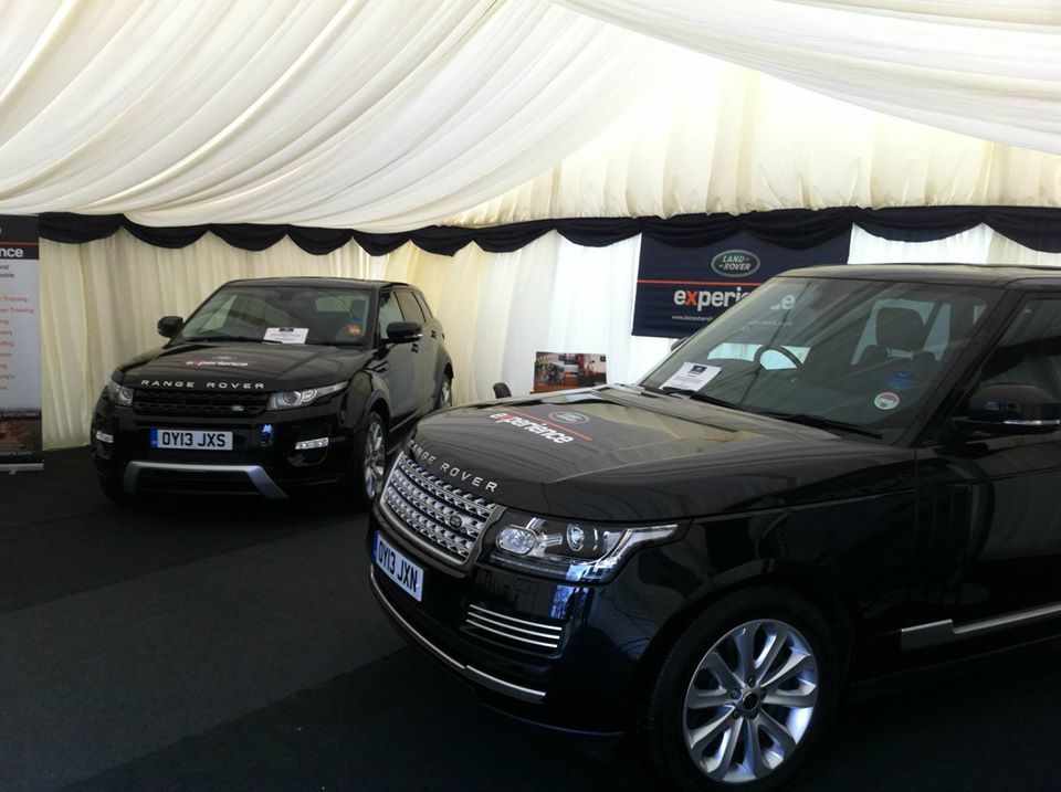 Two black Range Rover SUVs displayed under a white tent with a dark carpet; event setting.