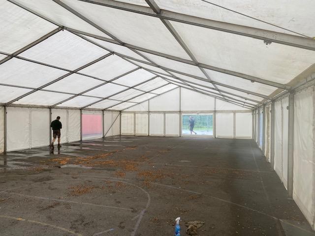 Large tent interior; person sweeping debris from the floor. White walls, translucent roof, metallic frame.