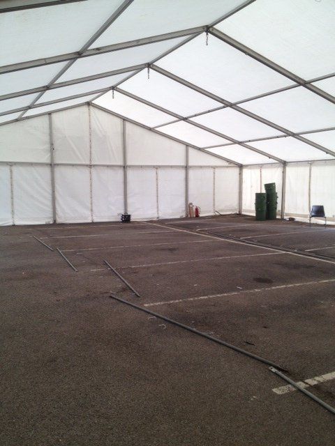 Empty white tent interior with asphalt floor and supporting metal beams.