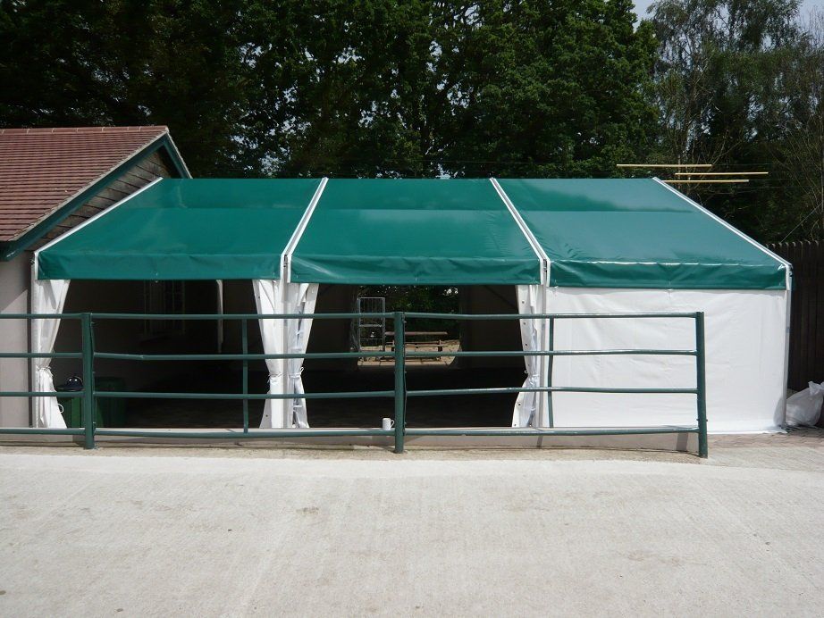 Green and white tent structure with open sides, and a black metal fence, on a concrete surface.