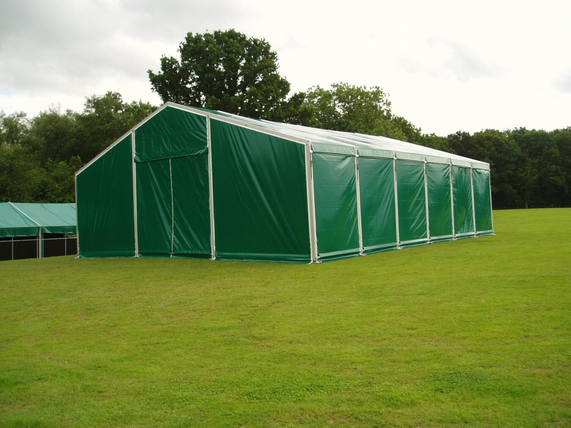 Green tent structure on a grassy field, trees in the background, overcast sky.