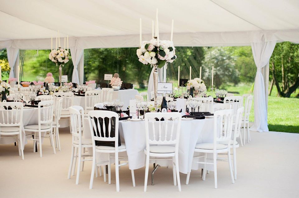Elegant white tent interior with round tables, chairs, and floral centerpieces, set for an event.