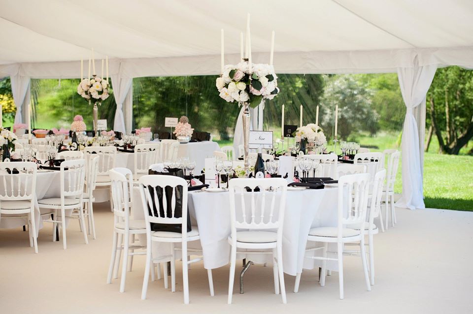 Elegant wedding reception tent with round tables, white chairs, and floral centerpieces.
