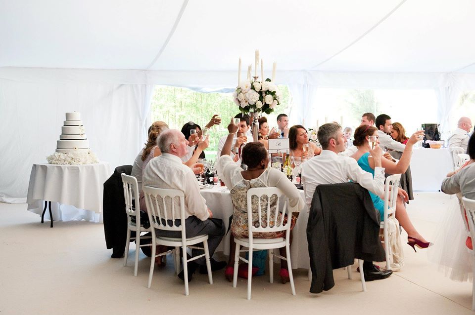 People at a wedding reception, toasting at a round table, cake in background.