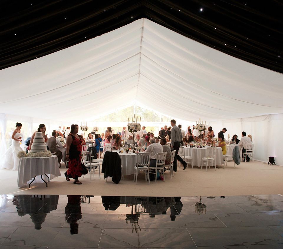 Wedding reception inside a white tent, guests at round tables, mirrored floor.