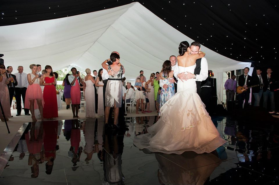 Bride and groom dancing at wedding reception. Guests watch on shiny dance floor in tent.