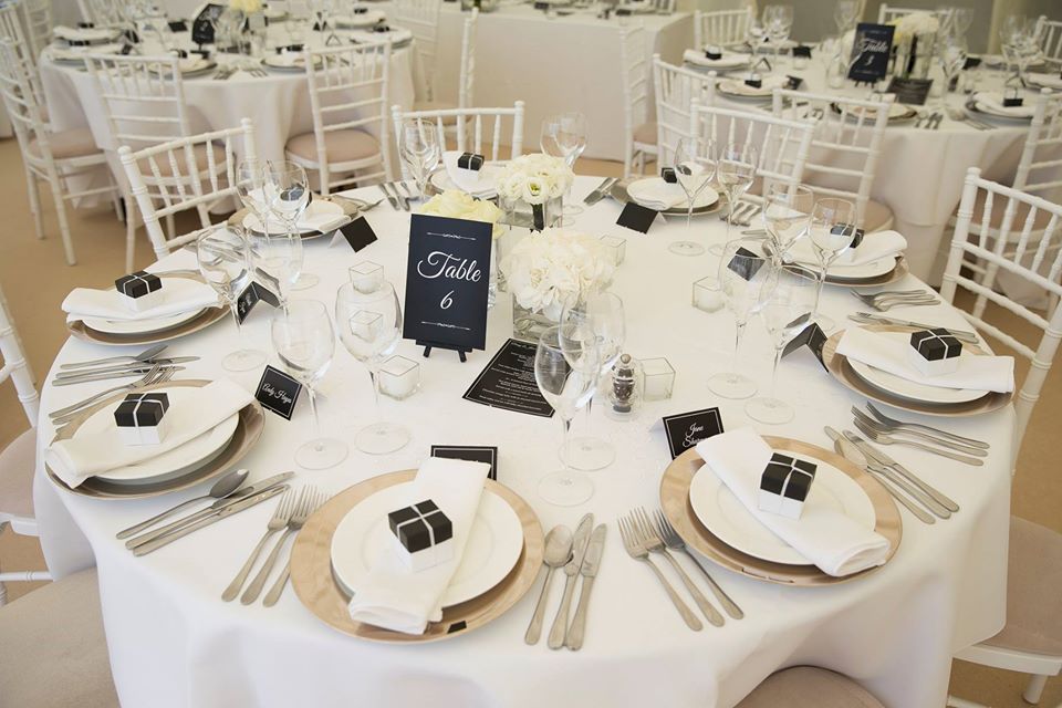 Round table set for a formal event, with white linens, gold chargers, and place settings.