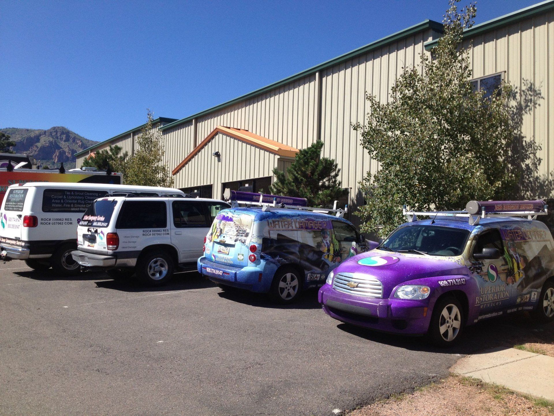 Several company vans parked in front of a building on a sunny day.