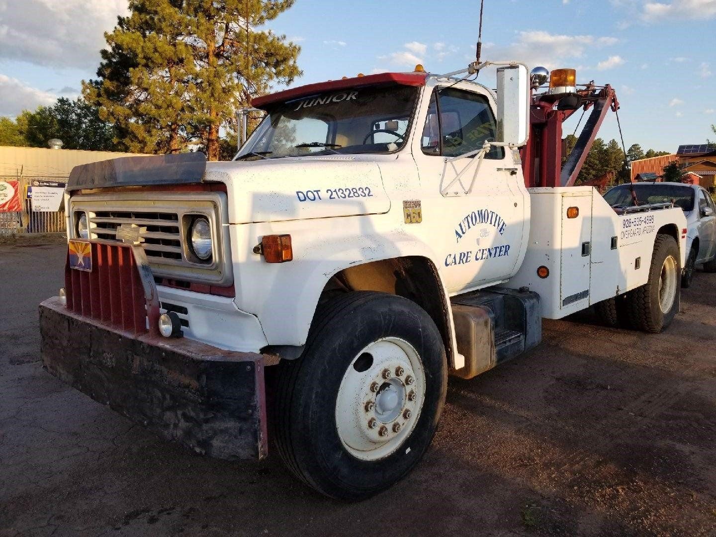 A white vintage Chevrolet tow truck with red trim parked on a gravel lot under a bright, partly cloudy sky.