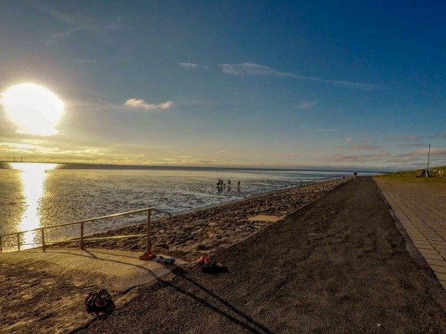 Bei Sonnenuntergang liegt eine Angelrute am Strand neben einem Gewässer.