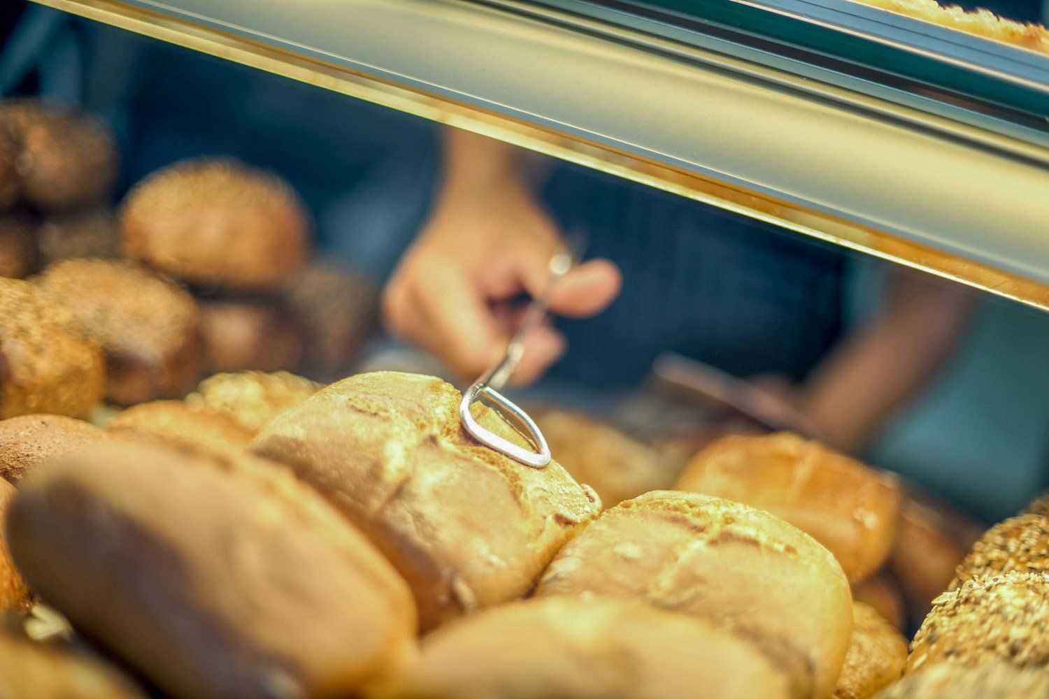 Eine Person nimmt ein Stück Brot aus einer Auslage in einer Bäckerei.