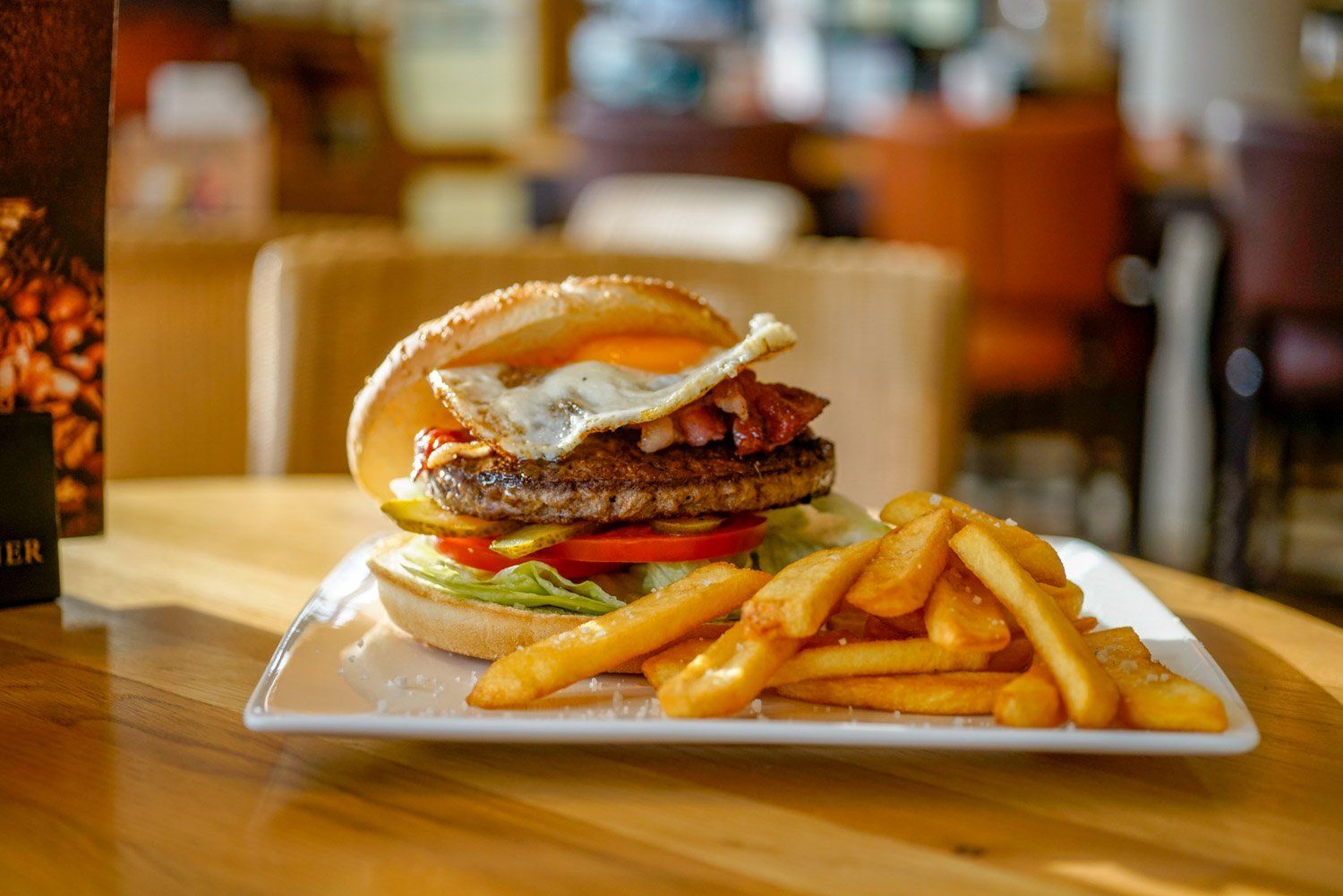 Ein Hamburger und Pommes Frites auf einem weißen Teller auf einem Holztisch.