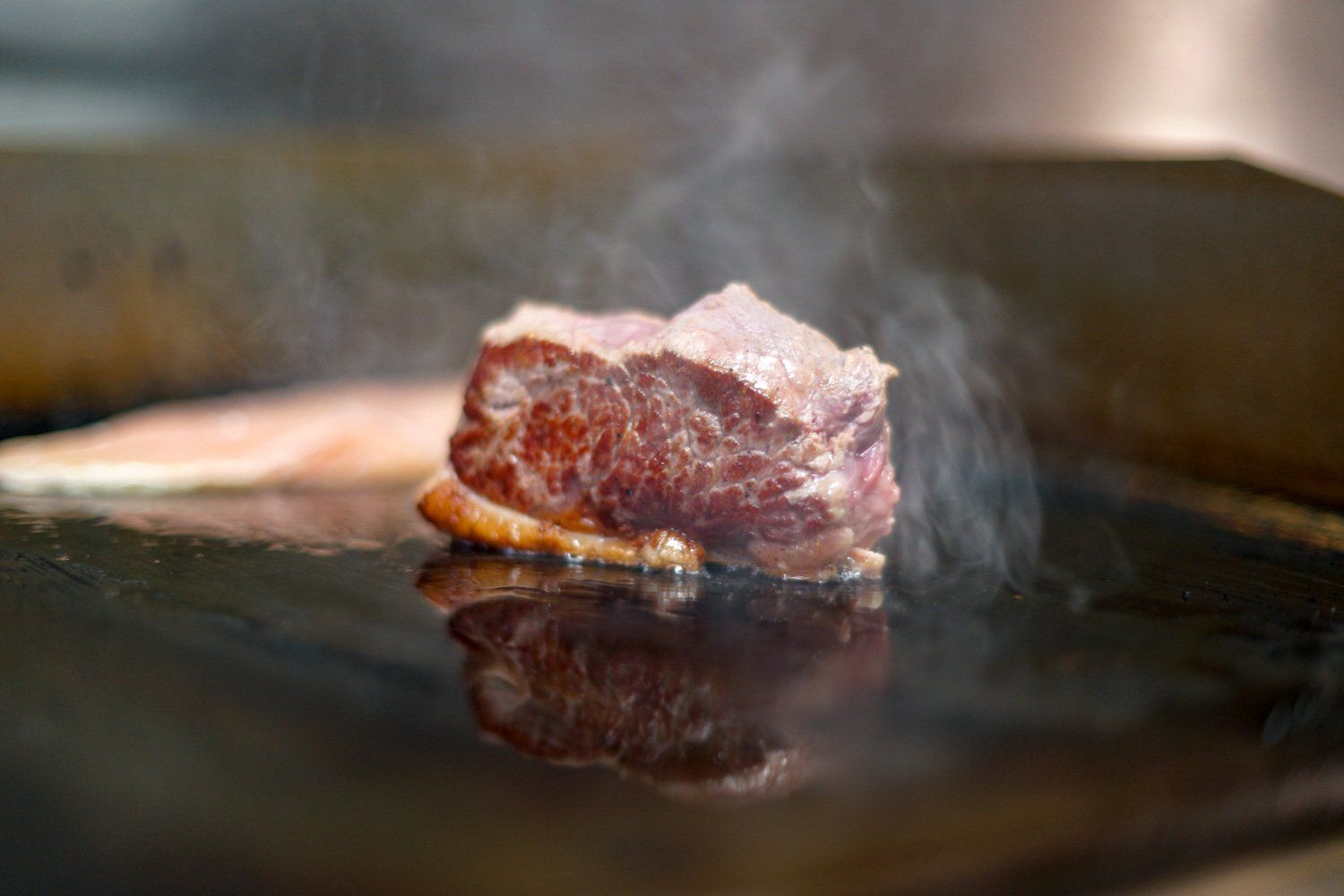 Auf einem Grill wird ein Stück Fleisch zubereitet.