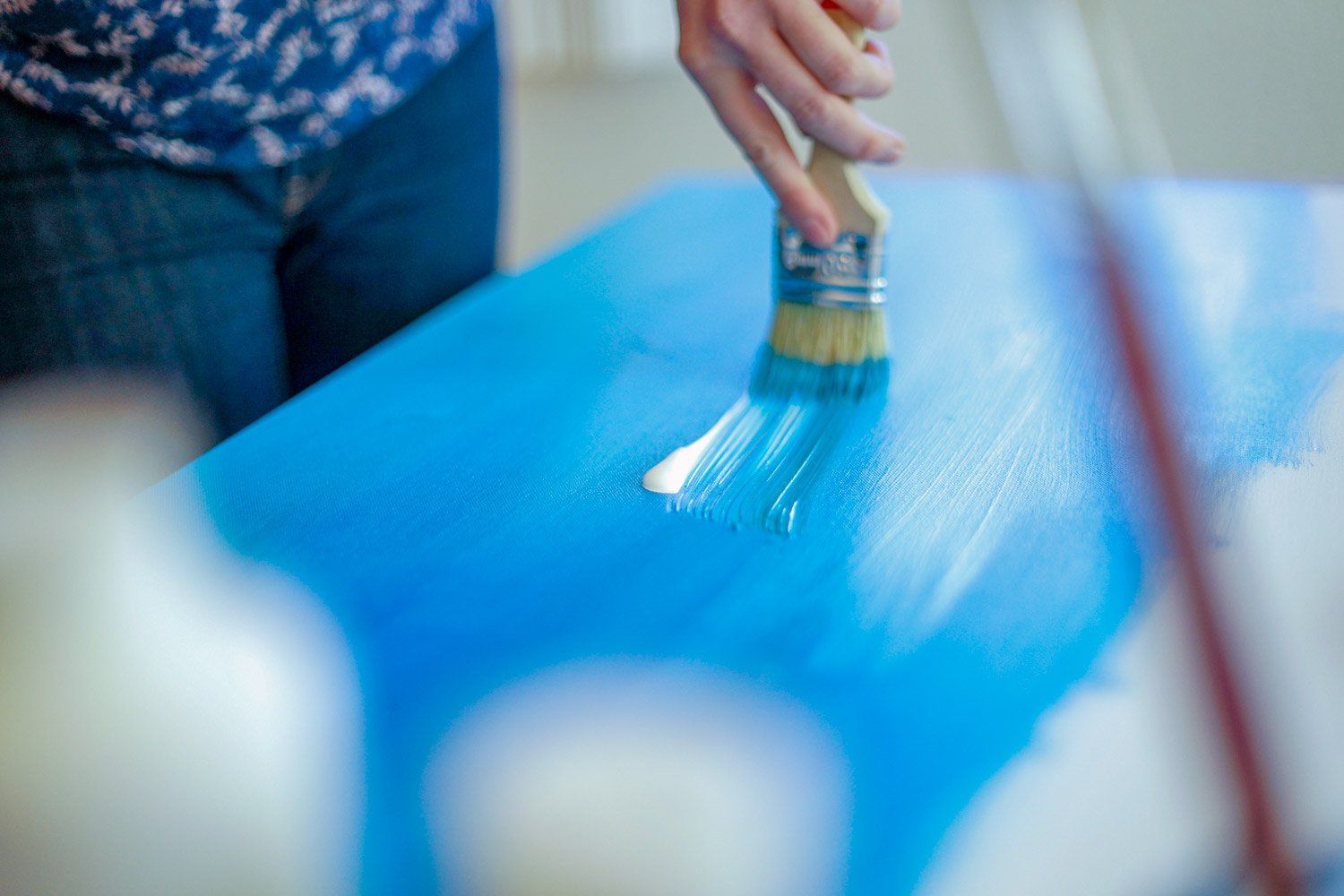 Eine Person streicht mit einem Pinsel einen blauen Tisch.