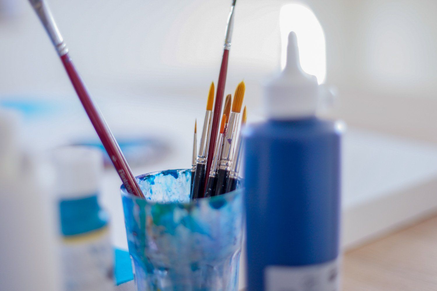 Ein mit Farbe gefülltes Glas und Pinsel neben einer Flasche blauer Farbe.