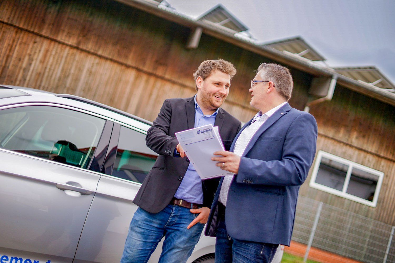 Zwei Männer stehen neben einem Auto und unterhalten sich.