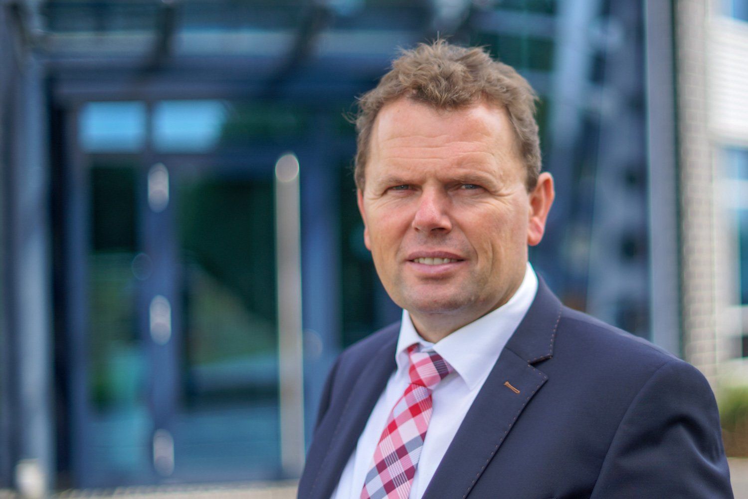 Ein Mann in Anzug und Krawatte steht vor einem Gebäude.