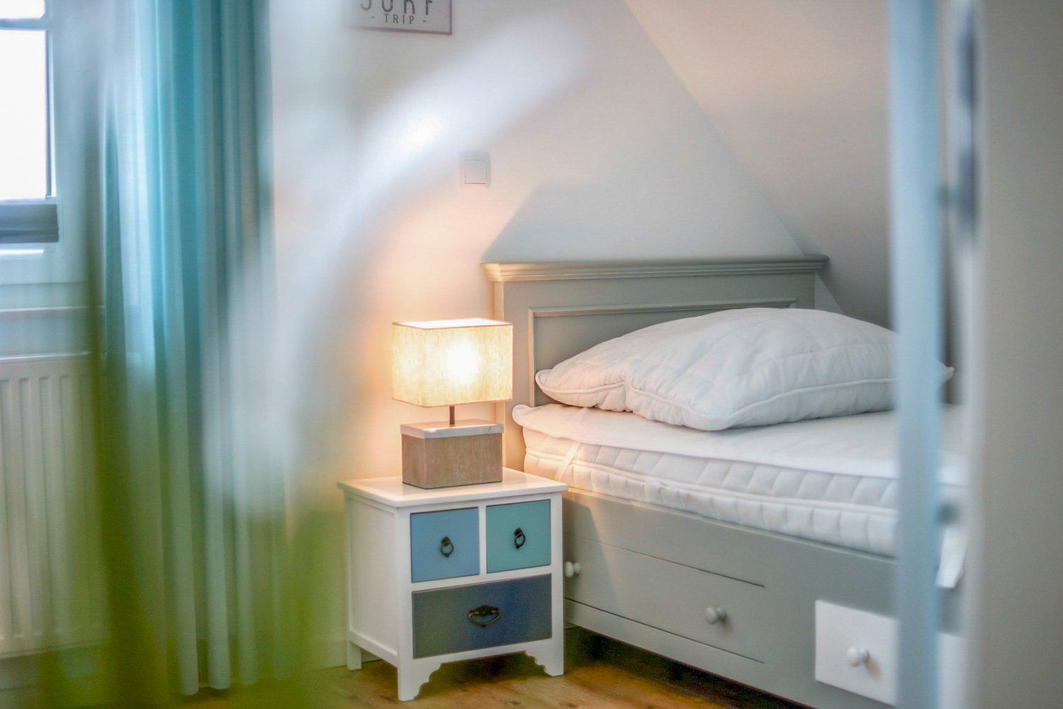 Ein Schlafzimmer mit Bett, Nachttisch, Lampe und Fenster.