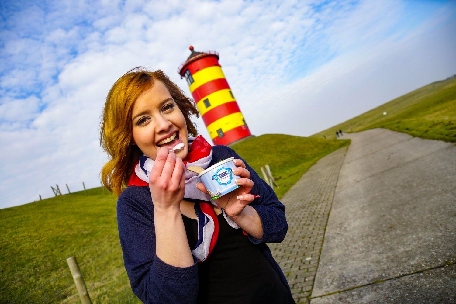 Eine Frau hält einen Becher Eis vor einem Leuchtturm.