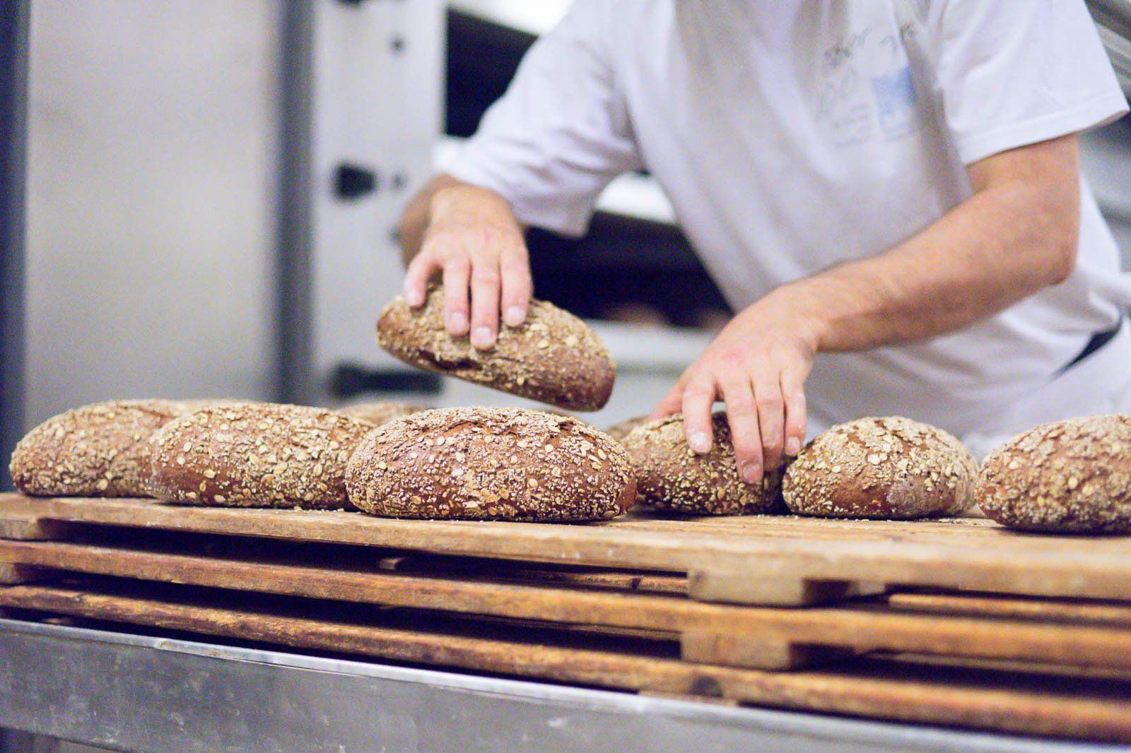 In einer Bäckerei schneidet ein Mann Brot auf einem hölzernen Schneidebrett.