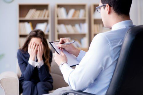 Specialista studiando la giovane seduta sul sofá che se copre la faccia
