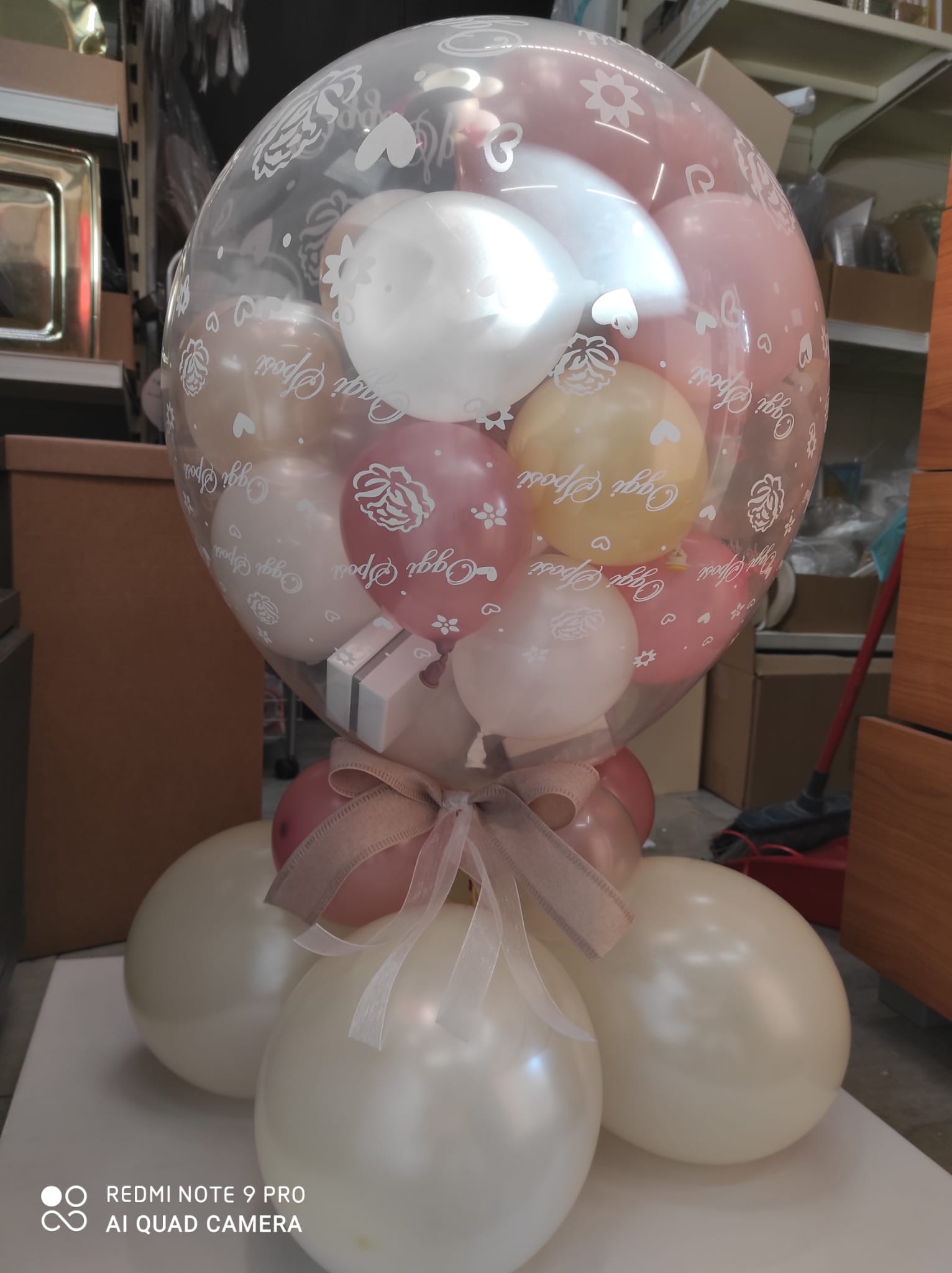 Bouquet di palloncini color pastello, fiocco e regalo all'interno di una bolla trasparente.