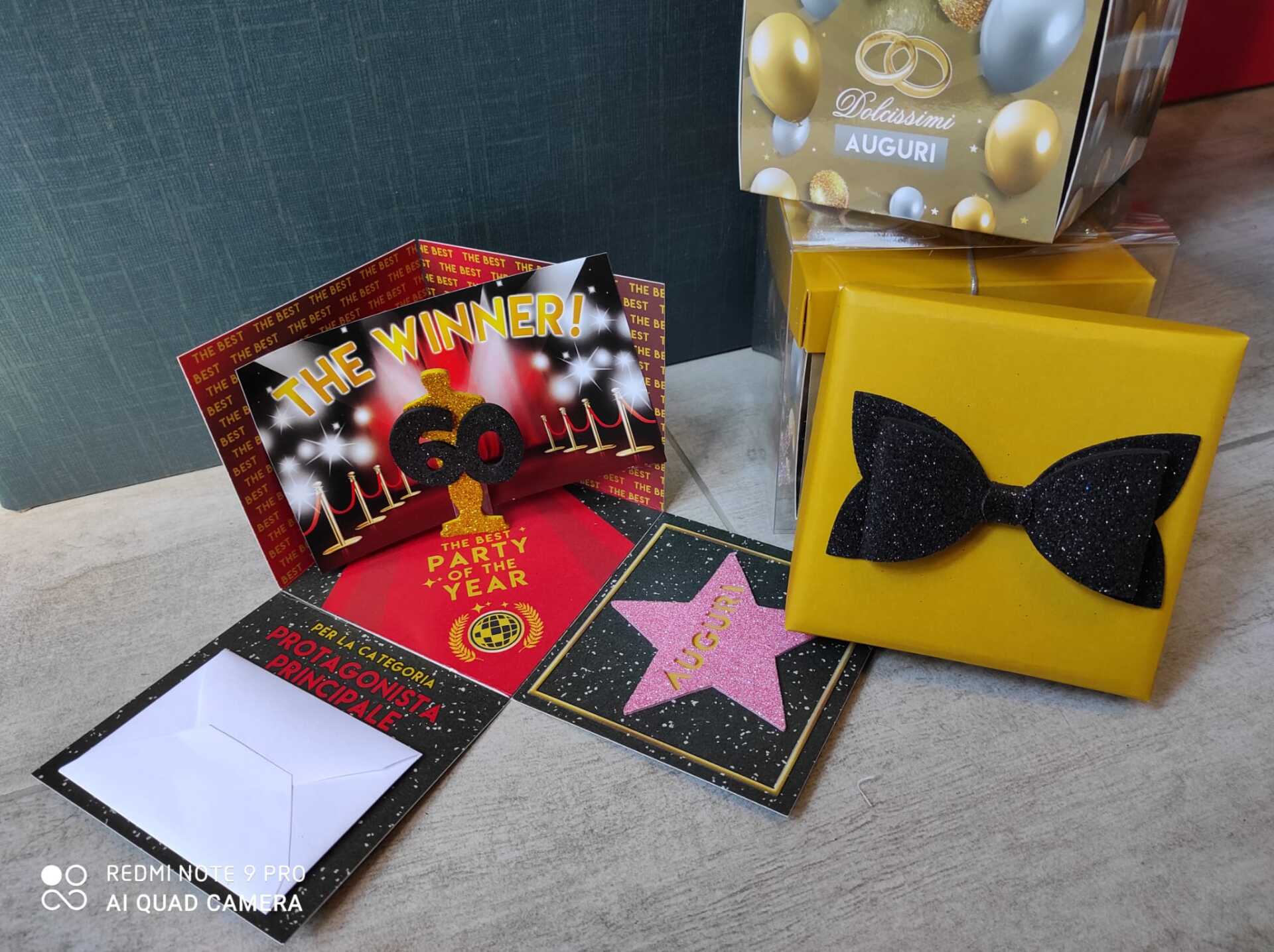 Scatola regalo gialla con fiocco nero accanto a un biglietto aperto e decorato per il 60° compleanno.