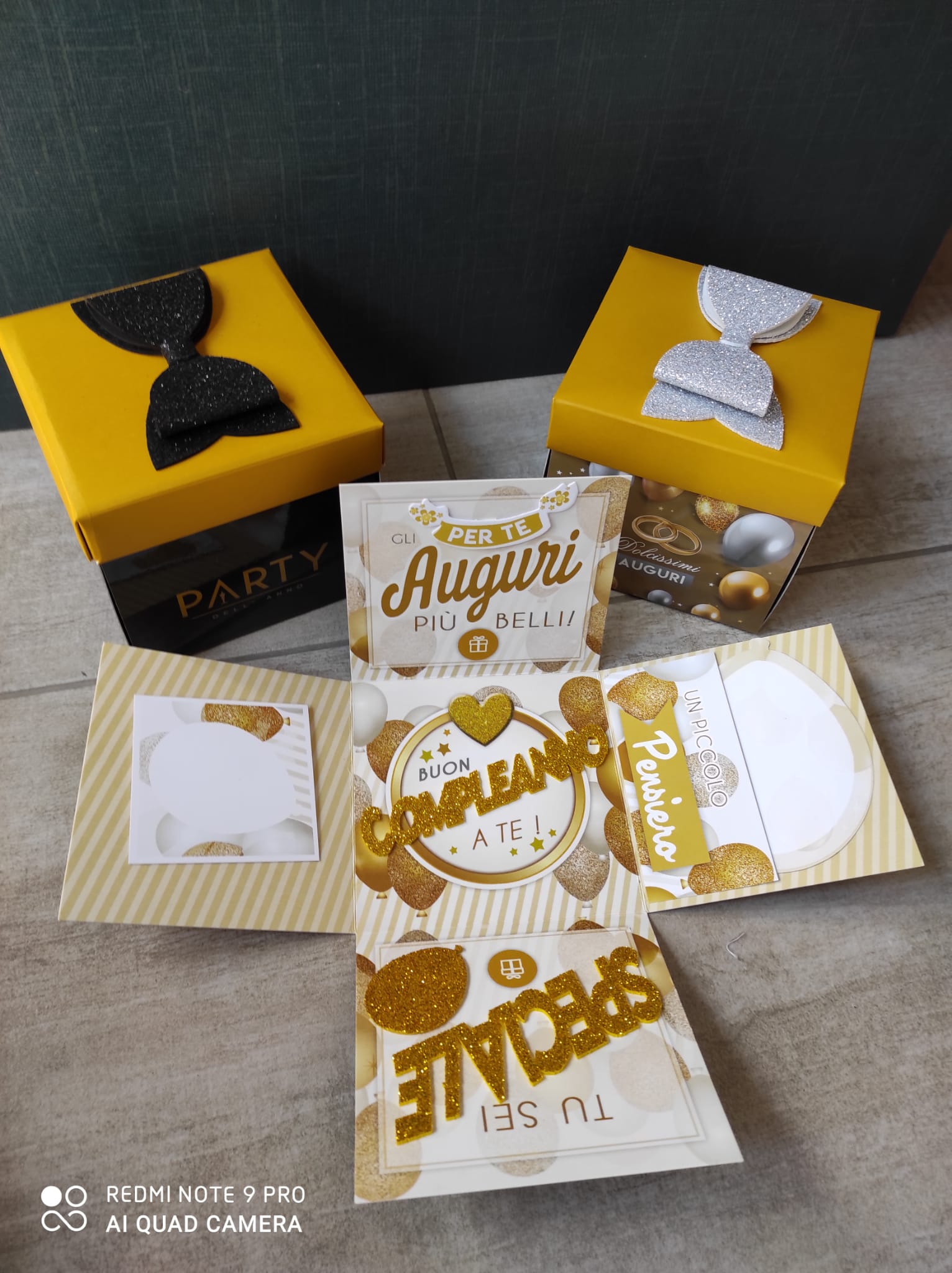 Scatola esplosiva per compleanno con dettagli in oro, nero e argento, che si apre rivelando auguri e decorazioni.