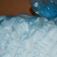 Noccioline bianche da imballaggio che riempiono una scatola, con un sacchetto di plastica blu sullo sfondo.
