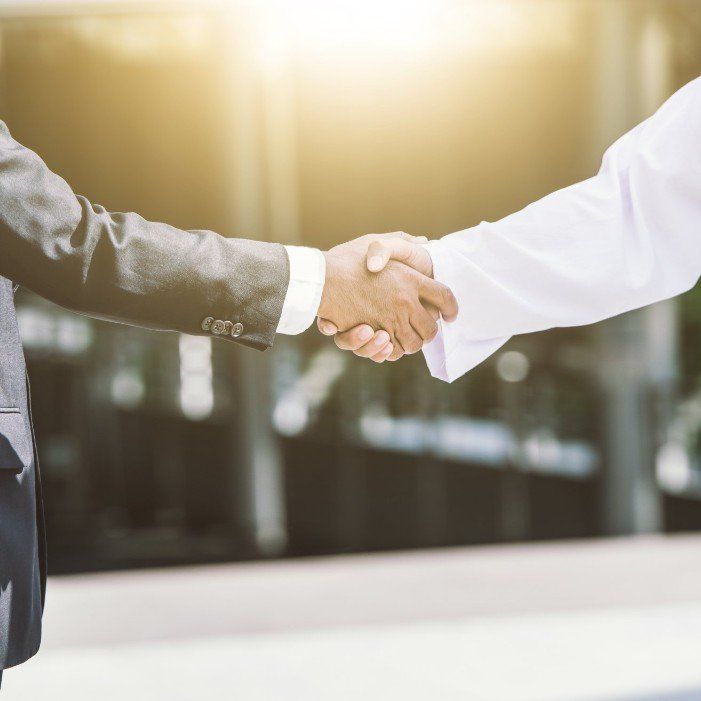 A man in a suit and a man in a white shirt are shaking hands.