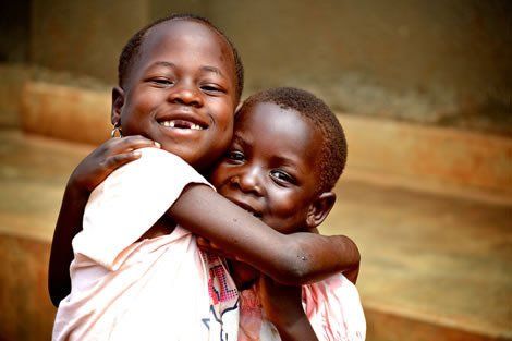 Two smiling Black children hugging. One child has a missing tooth.