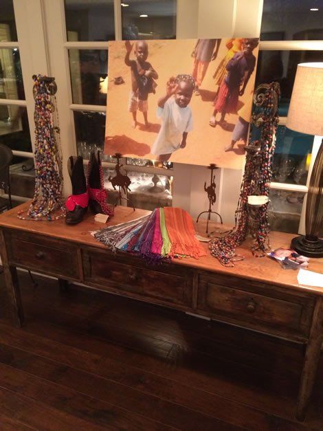 Wooden table with artwork, jewelry, and scarves. People in photo on the wall.