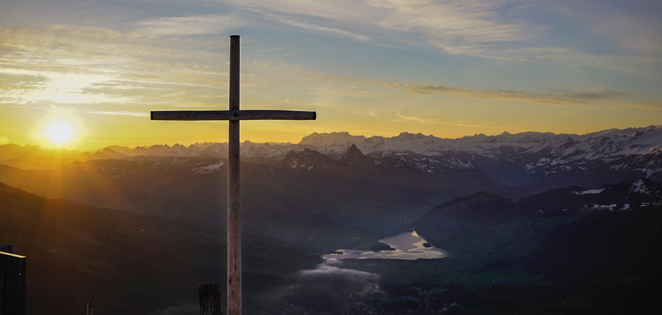 A cross in the foreground with mountains in the background.