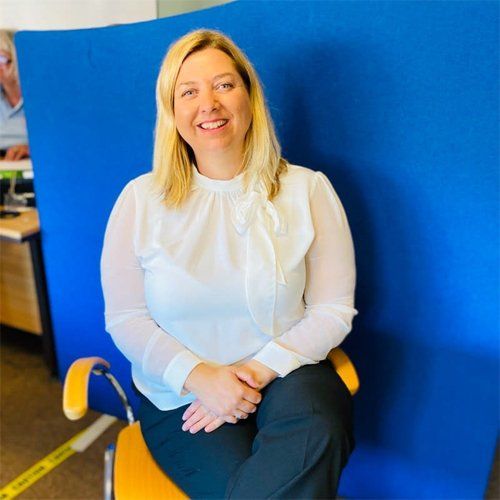A woman in front of a blue backdrop sitting in a yellow chair