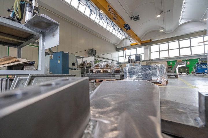 Officina industriale con macchinari di grandi dimensioni, materiali imballati e gru a ponte in un magazzino luminoso.