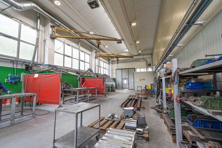 Luminosa officina industriale con scaffalature metalliche, attrezzature rosse e utensili su un pavimento di cemento.