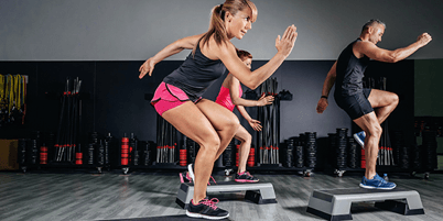 A group of people are doing step exercises in a gym.