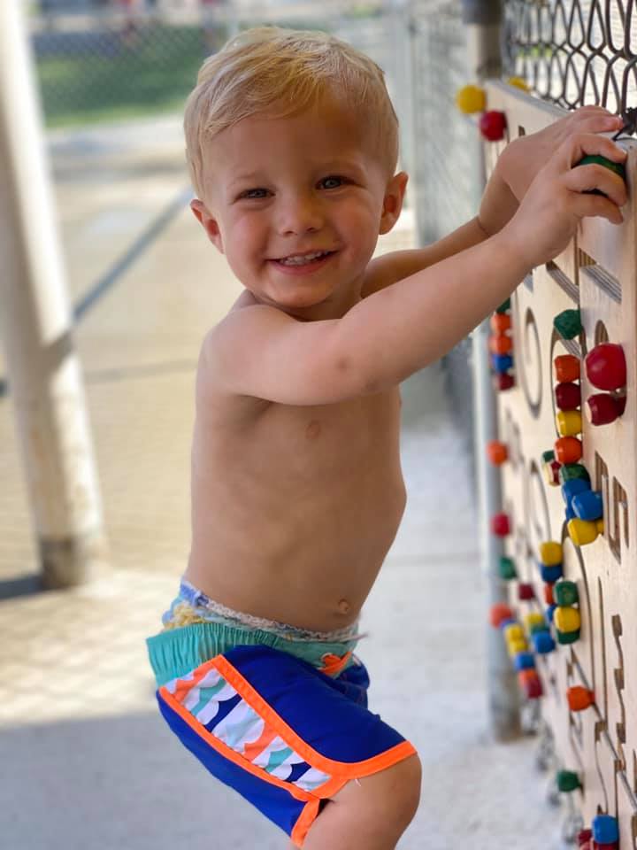 A young boy without a shirt is climbing a climbing wall