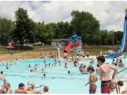 A group of people are swimming in a pool with a water slide in the background.