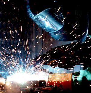 A man wearing a welding helmet is welding a piece of metal