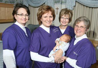 A group of women in purple scrubs holding a baby
