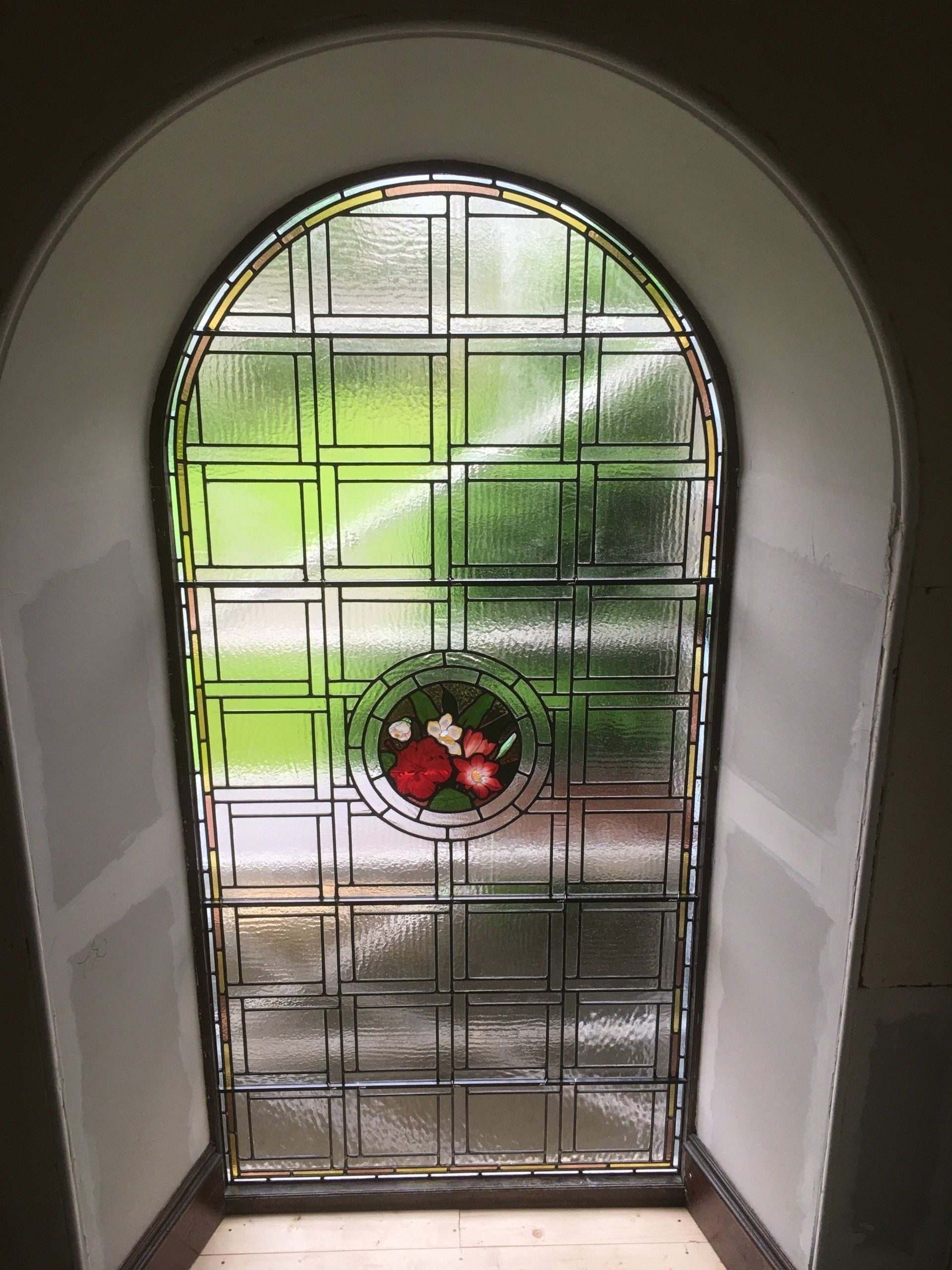 Arched frosted glass front door with a red floral wreath in a hallway