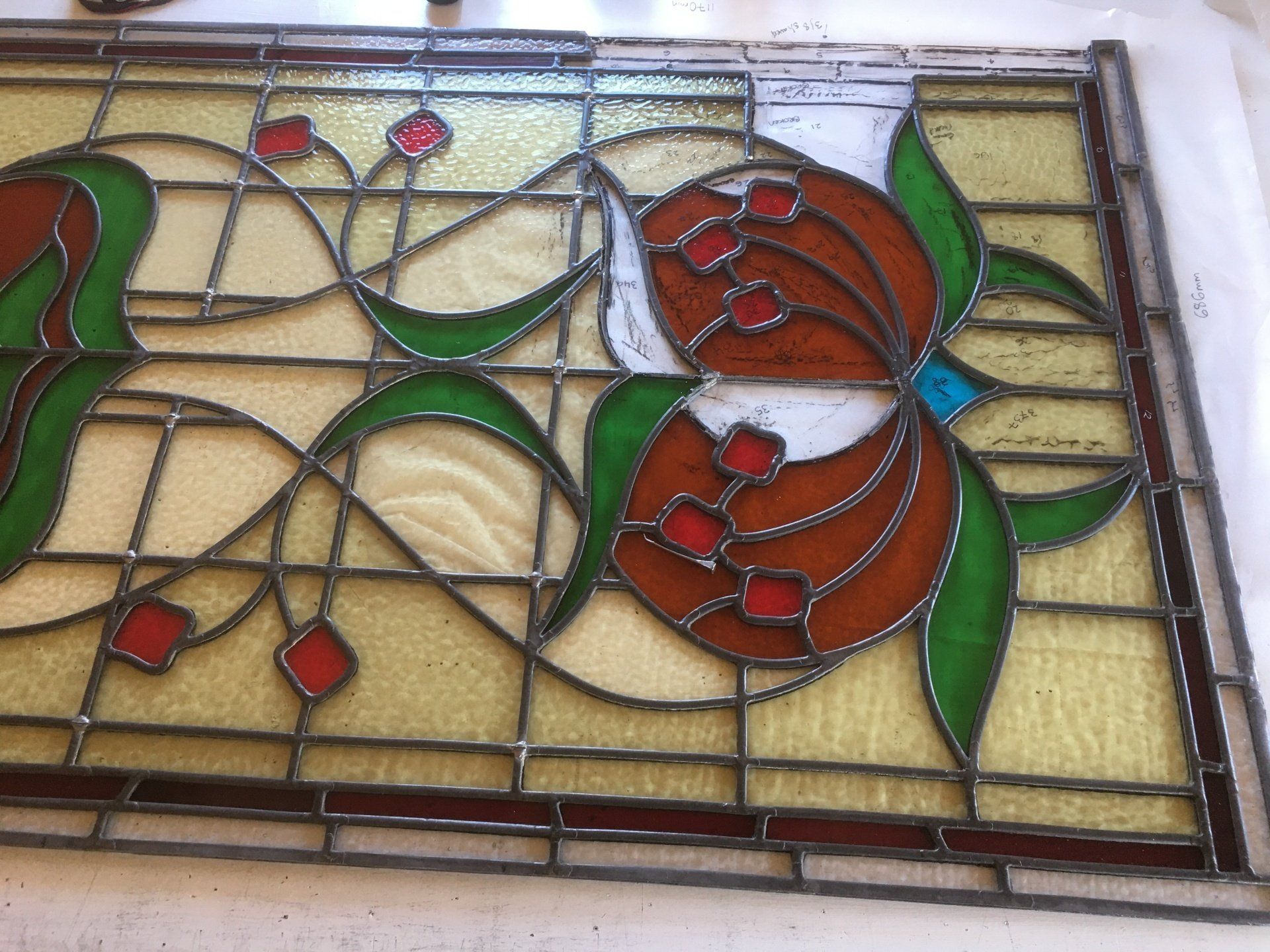 Stained-glass panel with red flowers, green leaves, and tan background in a decorative frame