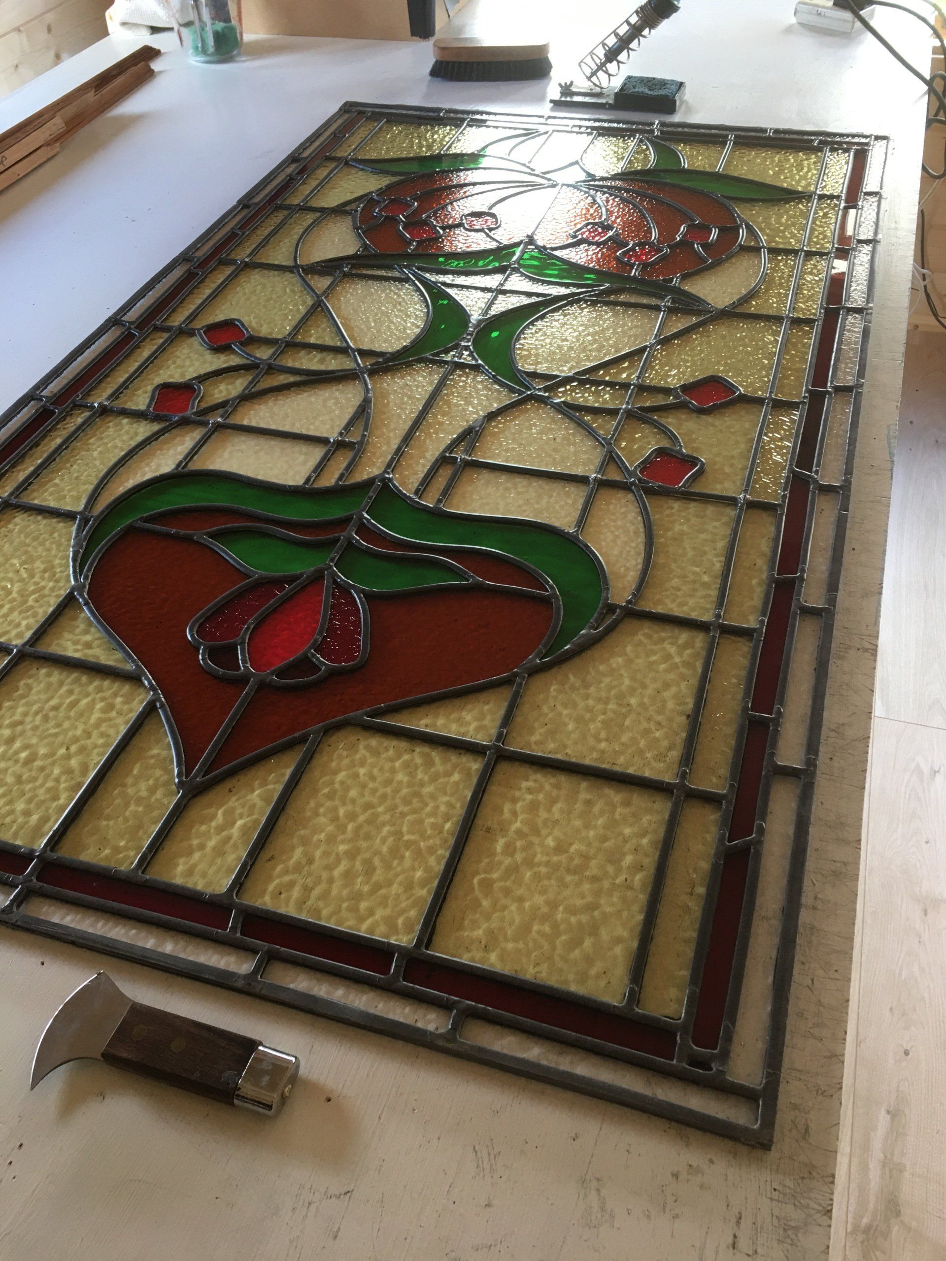 Stained glass panel with red, green, and cream floral design on a worktable